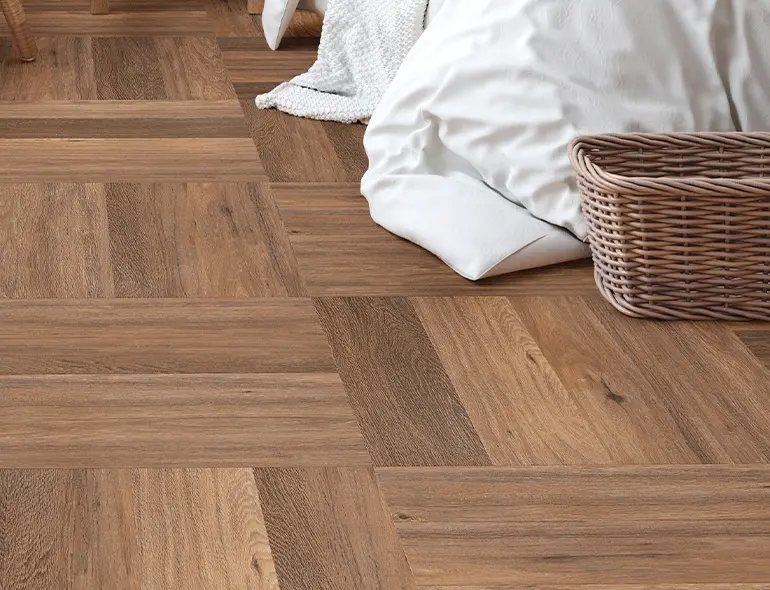  A corner of a bed and a basket on brown vinyl flooring